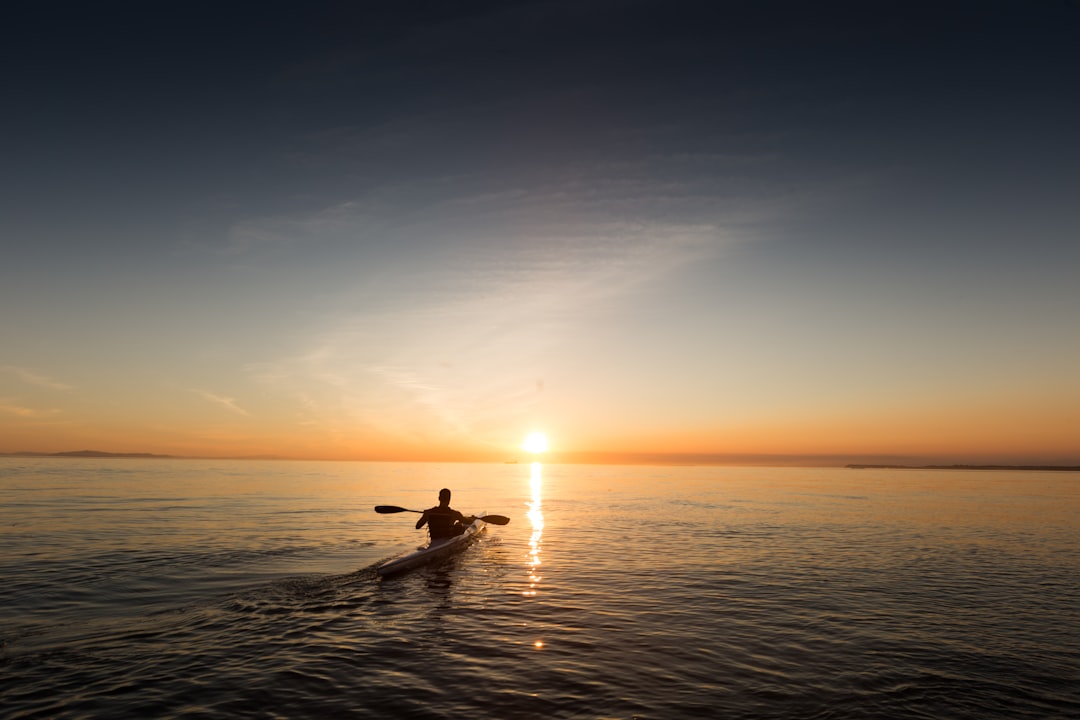 Silhouetted kayaker paddling calm water at sunset